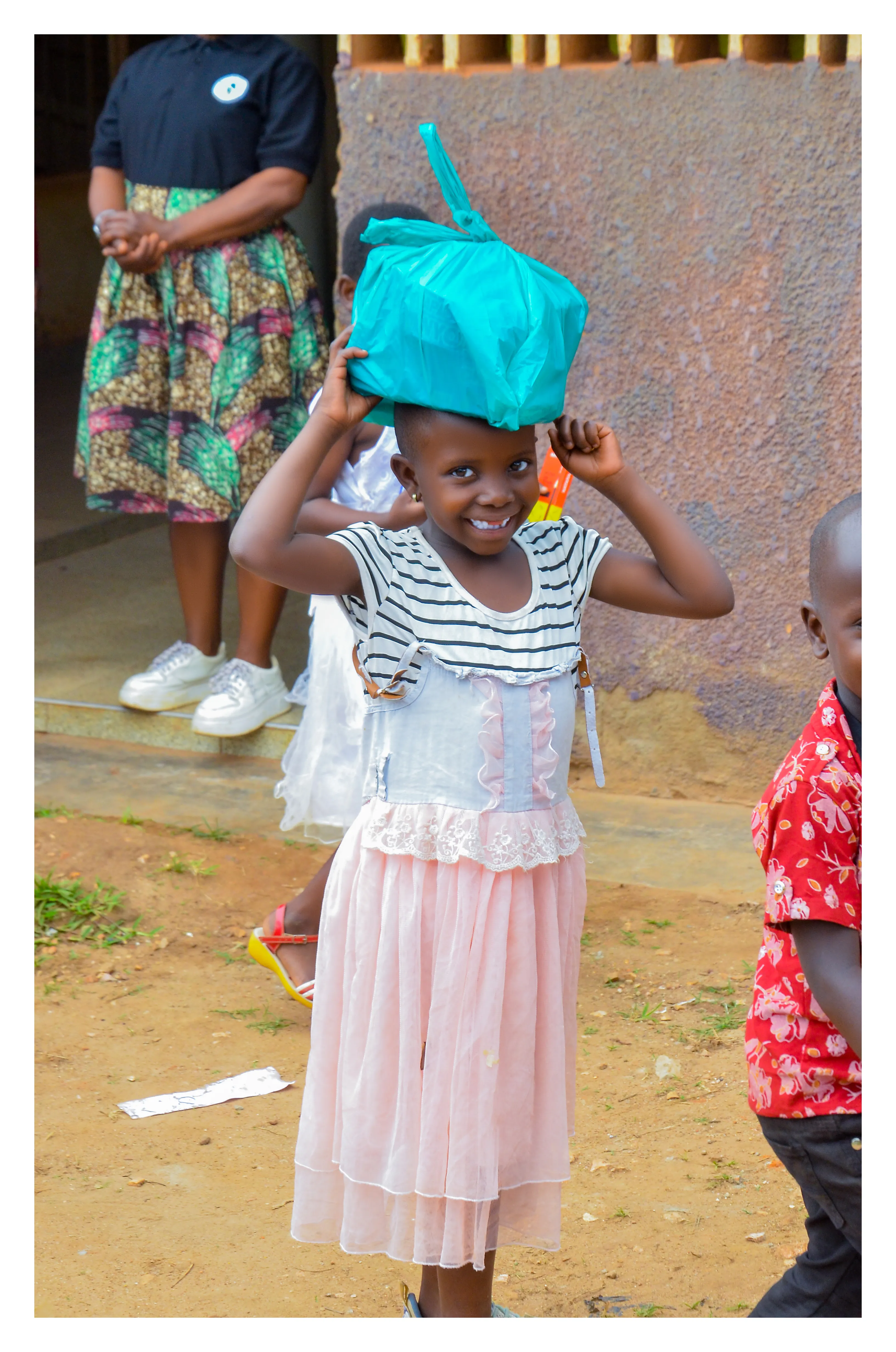 A smiling child carrying a food parcel on her head